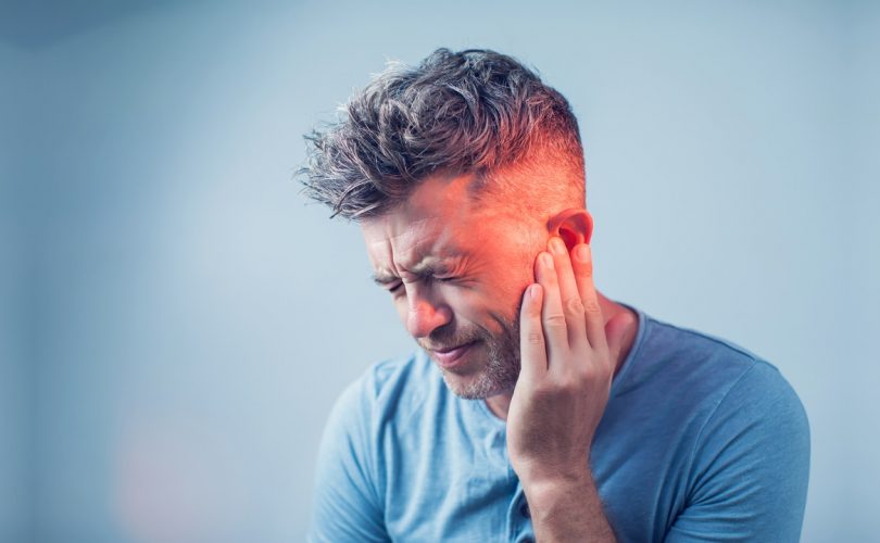 male having ear pain touching his painful head isolated on gray background